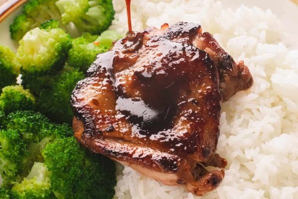 A budget-friendly take out meal with rice and broccoli served with a piece of meat on top.