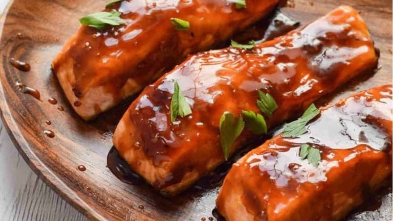 Main course for a dinner party - three perfectly grilled salmon fillets served on a rustic wooden plate.