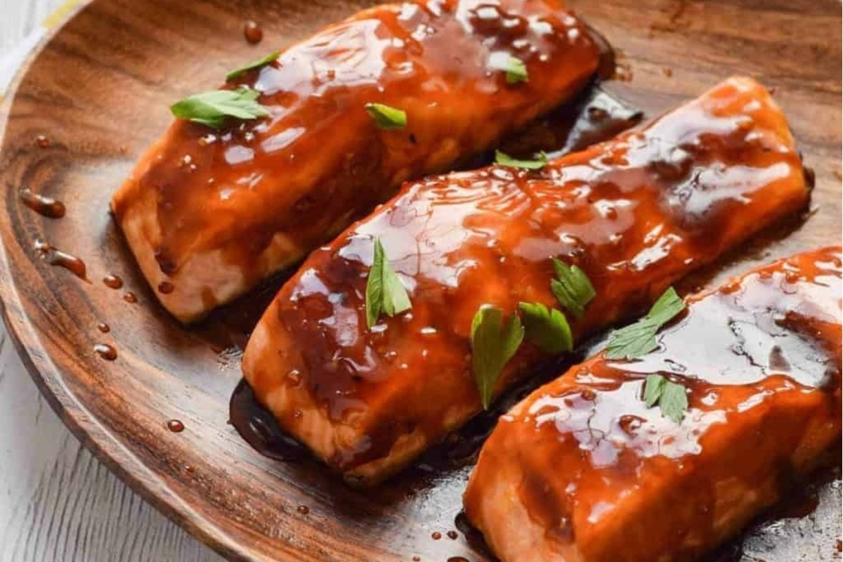 Main course for a dinner party - three perfectly grilled salmon fillets served on a rustic wooden plate.