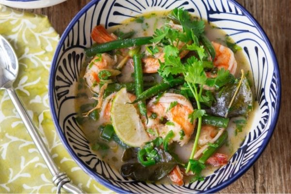 A bowl of seafood soup with shrimp and green beans, showcasing Asian flavors.