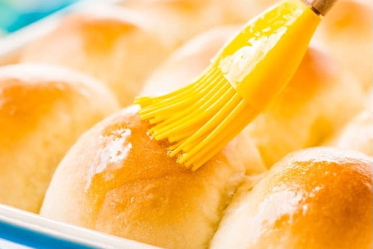 A yellow brush is being used to brush butter on a pan of cinnamon rolls, perfecting the delicious recipe.
