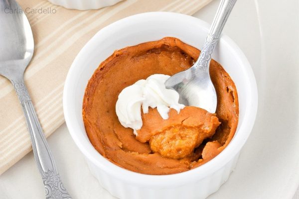 A bowl of pumpkin pudding with whipped cream and a spoon.