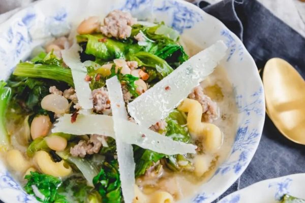 A bowl of pasta with meat and greens.