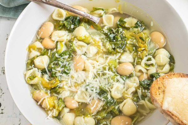 A bowl of pasta soup with green beans and bread.