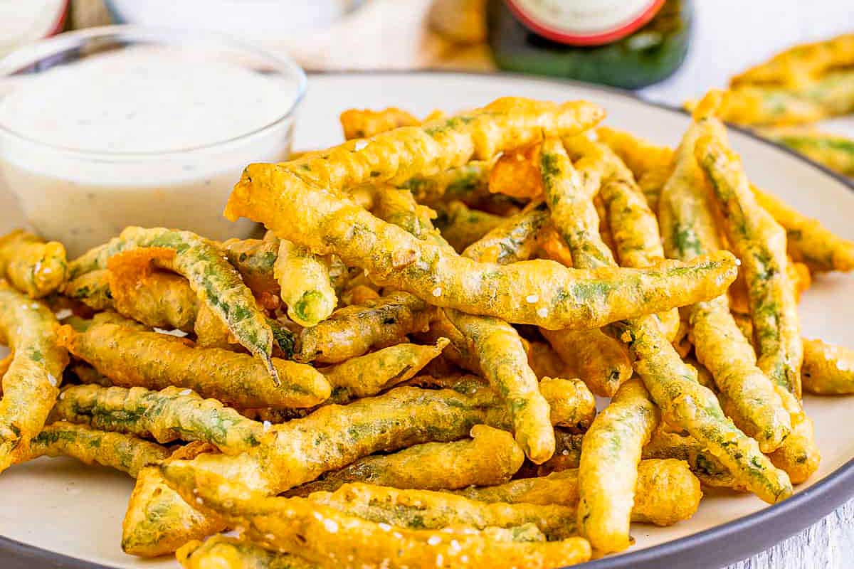 Fried green beans on a plate with dipping sauce.