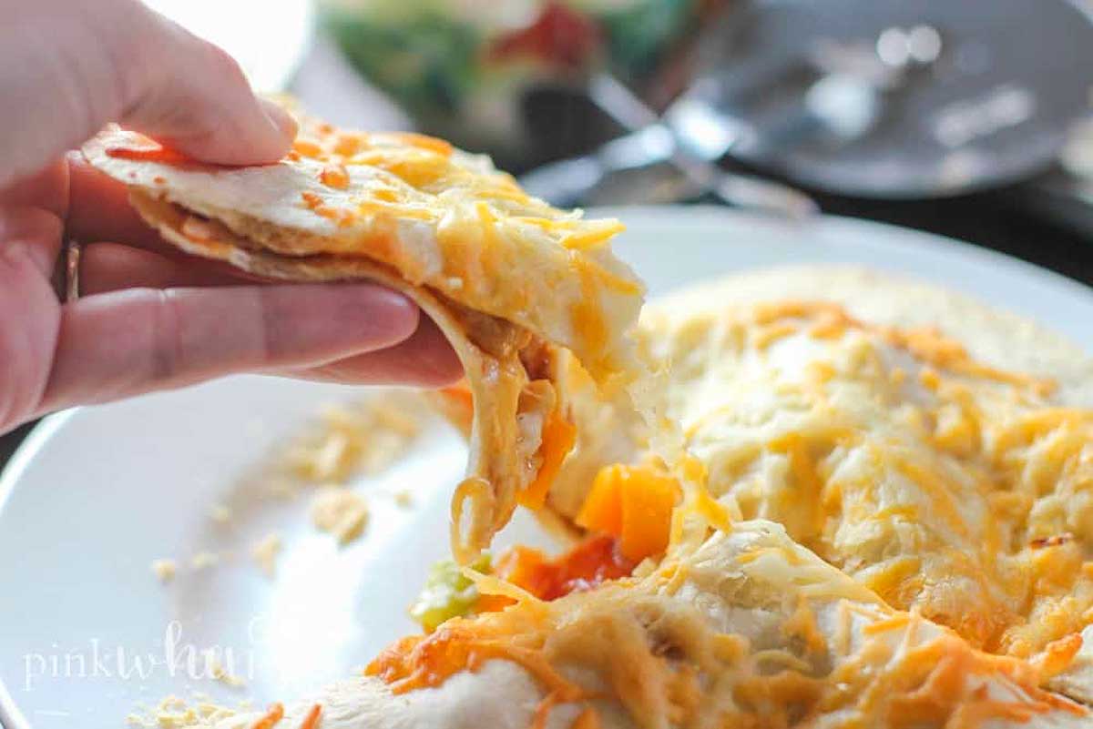 A person holding a piece of chicken quesadilla on a plate.
