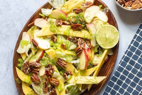 Colorful mango and pecan salad on a wooden plate.