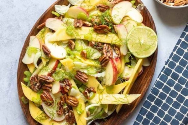 A salad with apples, pecans and pecans on a wooden plate.