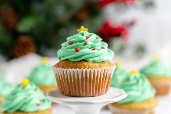 Christmas-themed cupcakes decorated with green frosting displayed on a white plate.