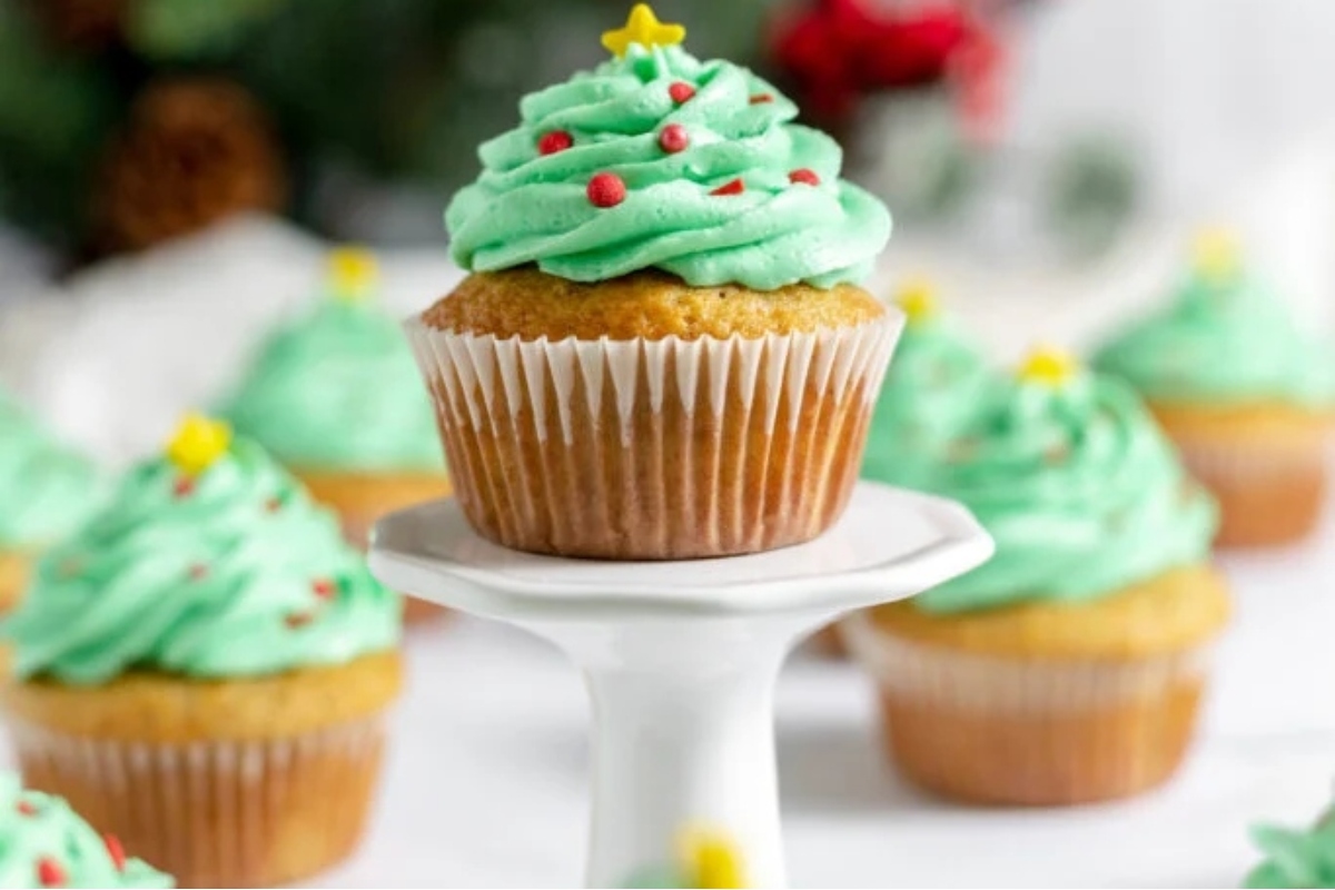 Festive Christmas cupcakes displayed on a white stand, adorned with vibrant green frosting.
