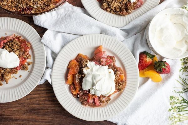 A plate of fruit crisp with whipped cream and berries.