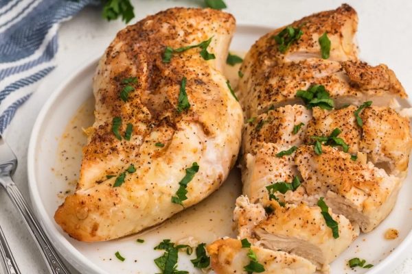 Two chicken breasts on a plate with parsley.