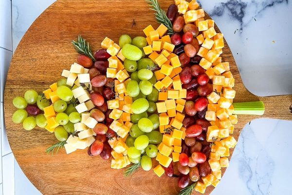 A platter of cheese, grapes and charcuterie on a wooden board.