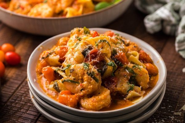 A bowl of pasta with shrimp and tomatoes.