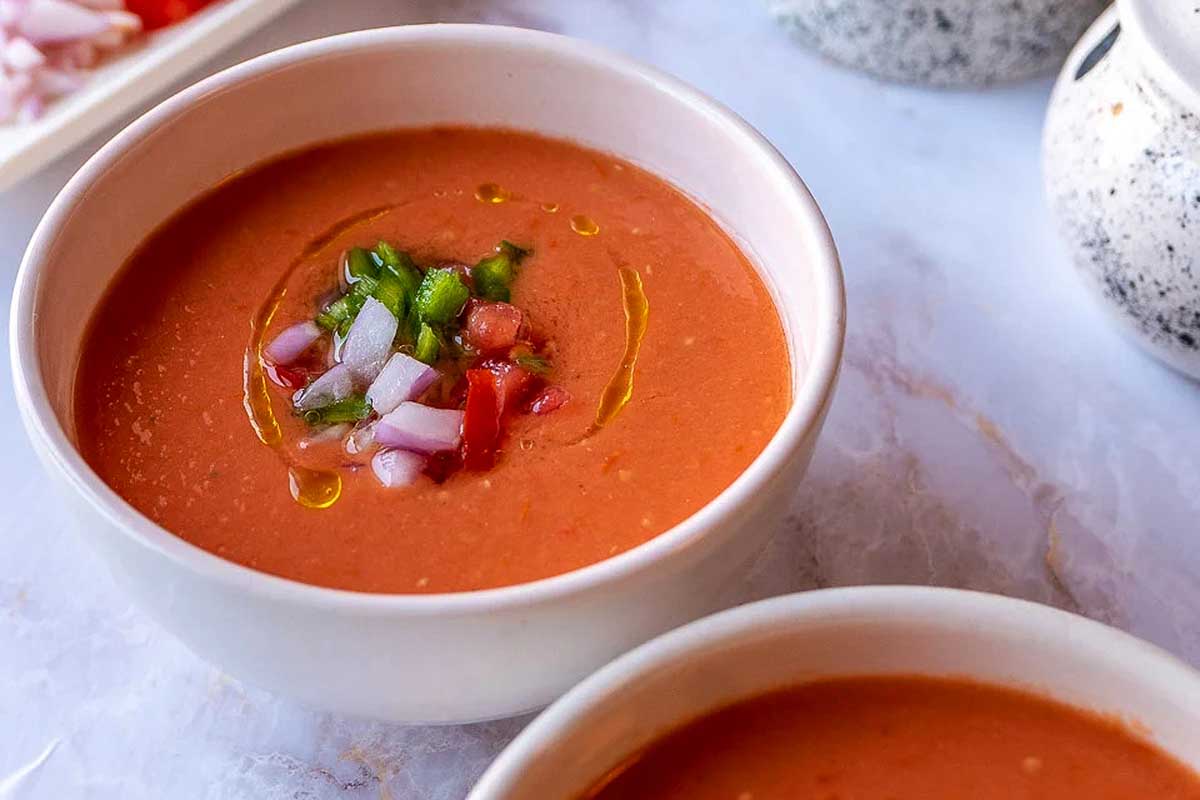 Two bowls of tomato soup with onions and peppers.