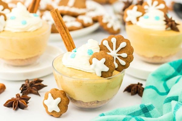 Gingerbread cheesecake in a cup with cinnamon sticks and gingerbread cookies.