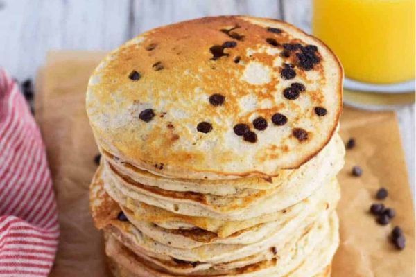 A stack of chocolate chip pancakes with a glass of orange juice.