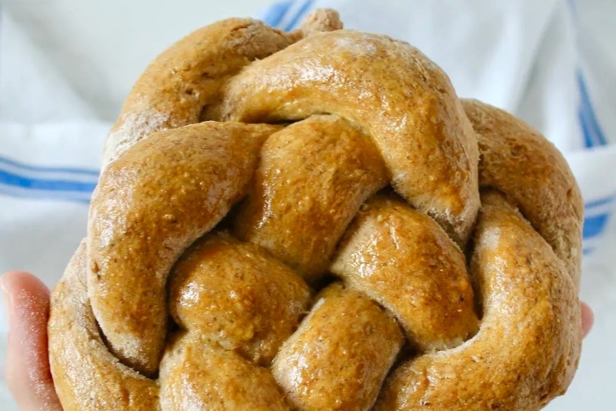 A person is holding a braided loaf of bread in a basket.