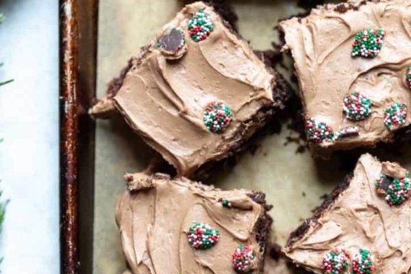 A tray of chocolate brownies with icing, adorned with sprigs of rosemary.