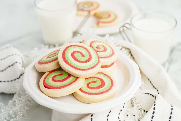 Christmas swirl cookies on a white plate with a glass of milk.