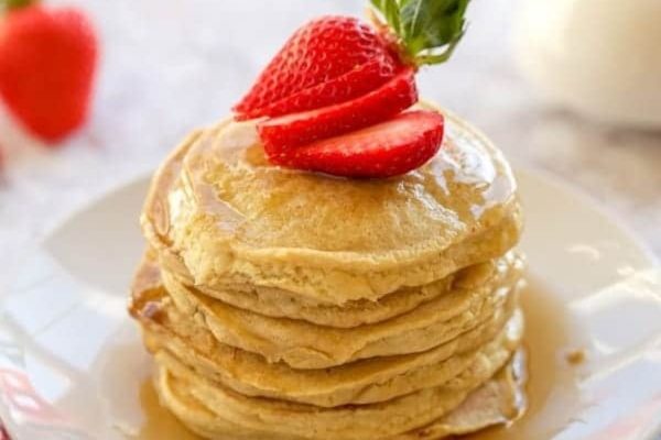 A stack of pancakes with strawberries and syrup on a plate.