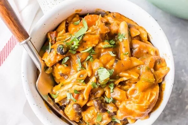 A bowl of chicken pasta in a white bowl with a spoon.