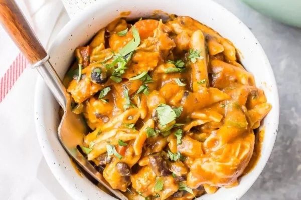 A delicious bowl of penne pasta in a flavorful sauce with a convenient spoon for easy eating.