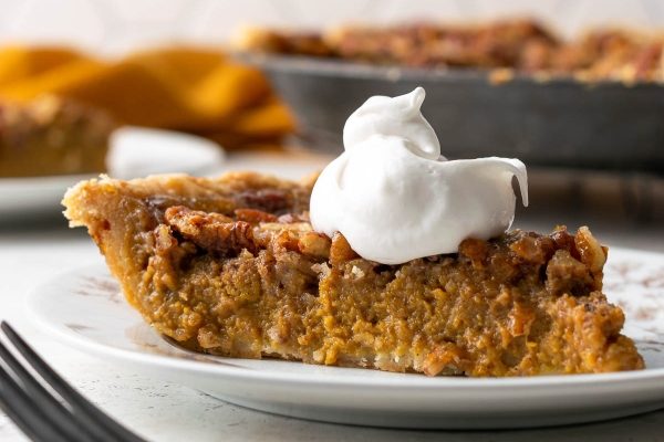 A slice of pumpkin pie with whipped cream on a plate.
