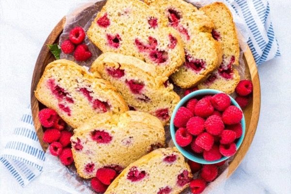 Raspberry bread on a wooden plate with raspberries.