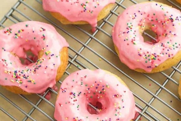 Pink glazed donuts with sprinkles on a cooling rack.