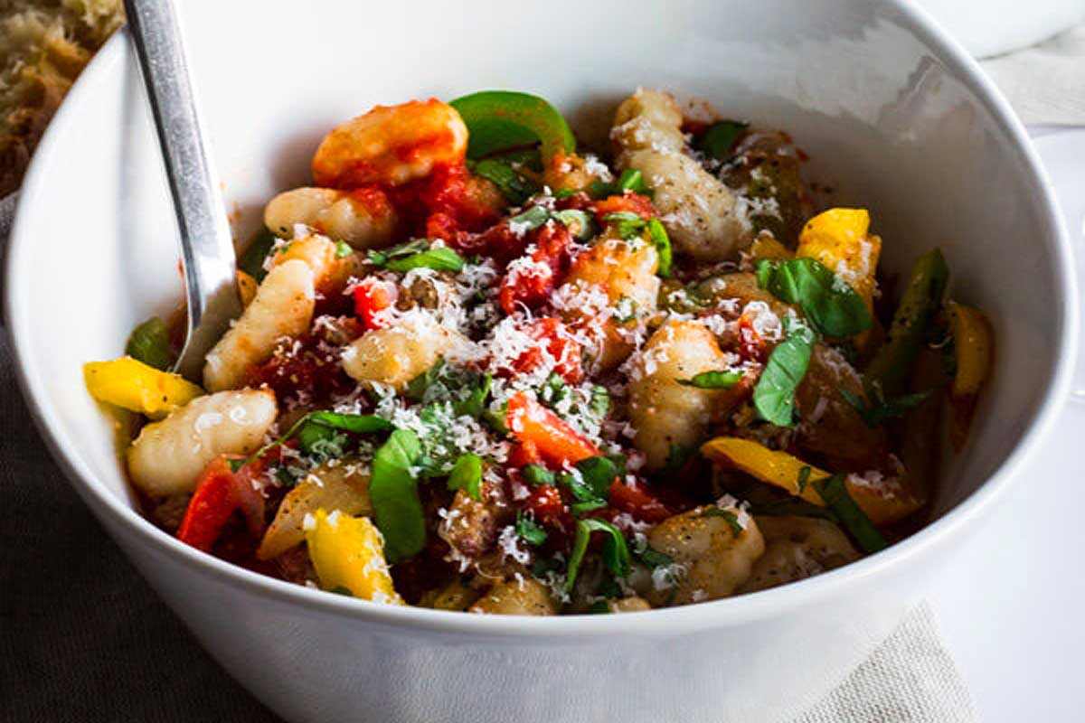 A white bowl filled with gnocchi and vegetables.