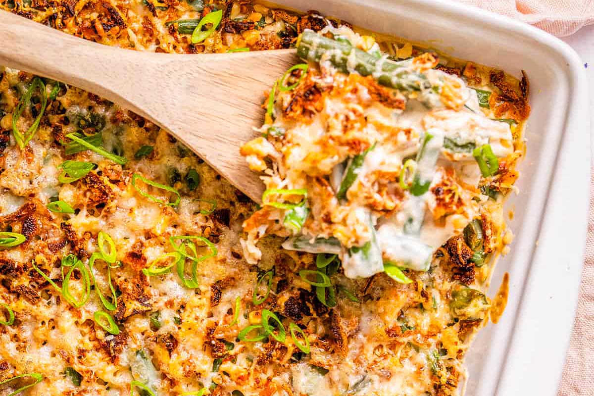 Green bean casserole in a casserole dish with a wooden spoon.