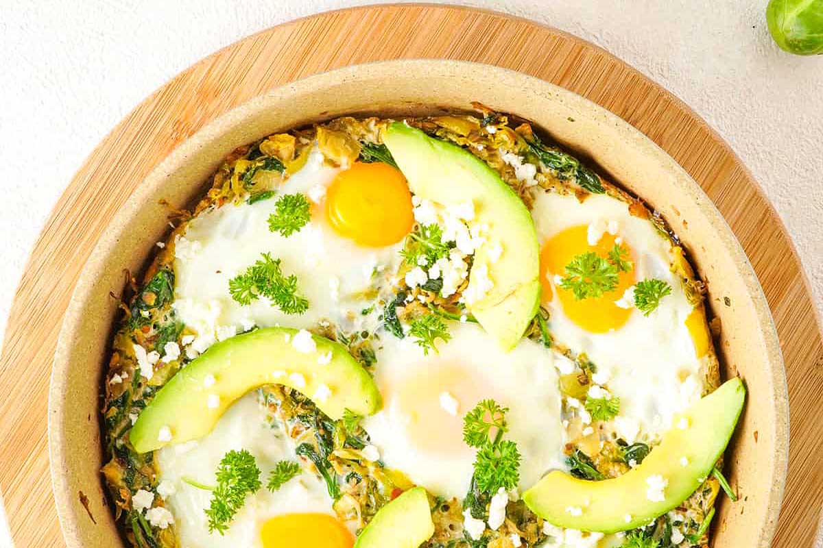 A quiche with eggs and avocado on a wooden board.