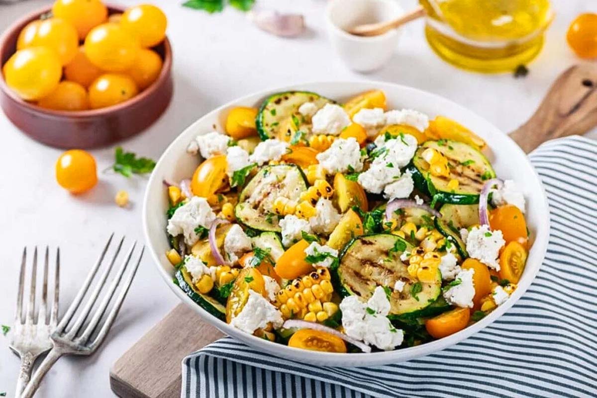 A bowl of grilled zucchini salad with feta cheese and tomatoes. Try this delicious zucchini recipe for a refreshing and healthy meal option.