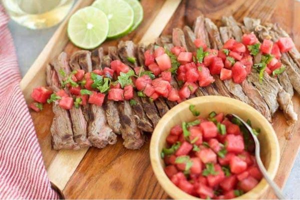 Grilled steak with watermelon salsa on a cutting board.