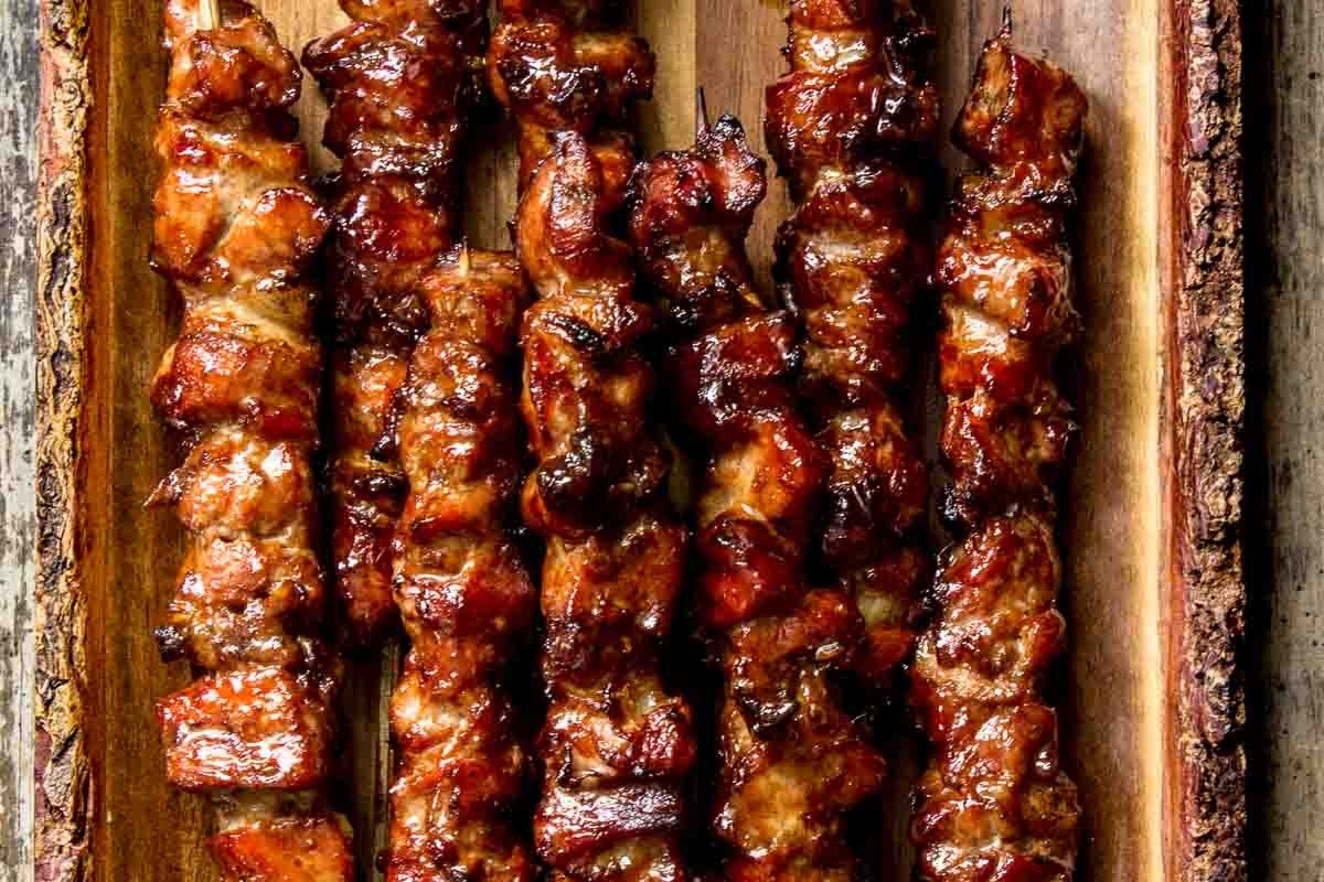 Grilled pork skewers on a wooden tray.