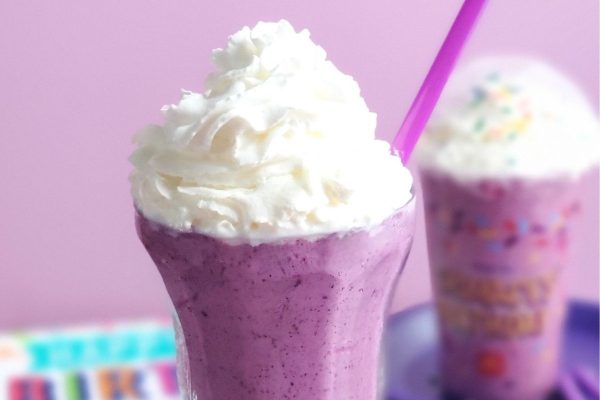 A purple smoothie with whipped cream and a purple straw, perfect for milkshake lovers.