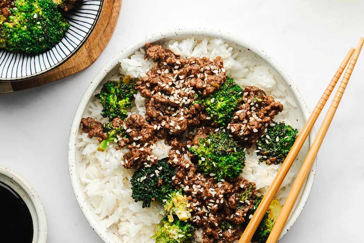 A bowl of beef, broccoli and rice with chopsticks.