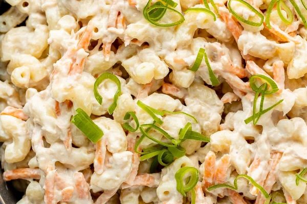 A bowl of macaroni salad with carrots and green onions.