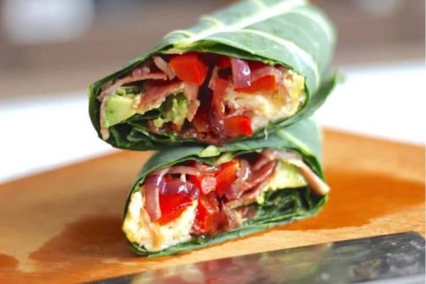 Two meal prep wraps with meat and vegetables on a cutting board.