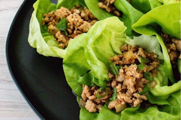 A plate of lettuce wraps with meat on it.