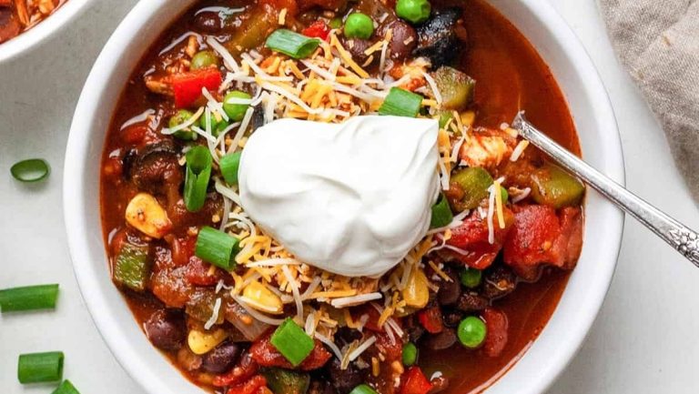 Chili in a bowl with sour cream and peas.