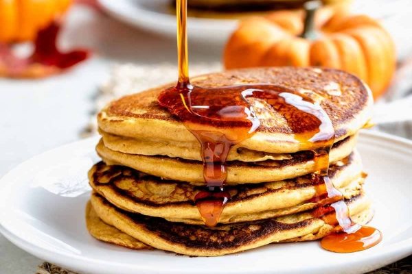 A stack of pumpkin pancakes being drizzled with maple syrup.