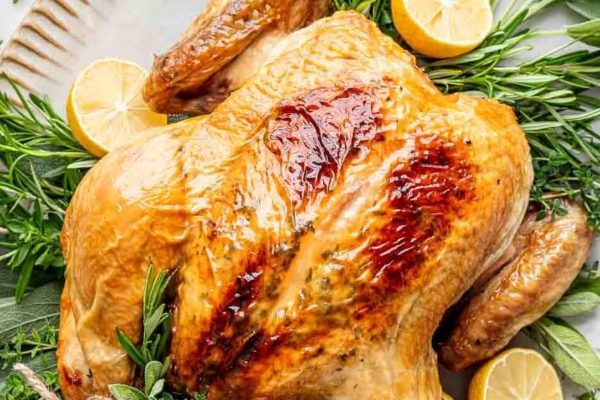 A roasted turkey with rosemary and lemon slices on a white plate.