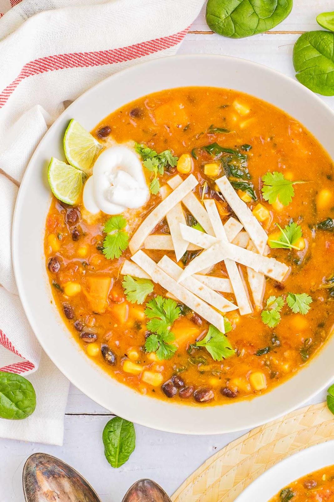 A bowl of mexican black bean soup with tortillas and sour cream.