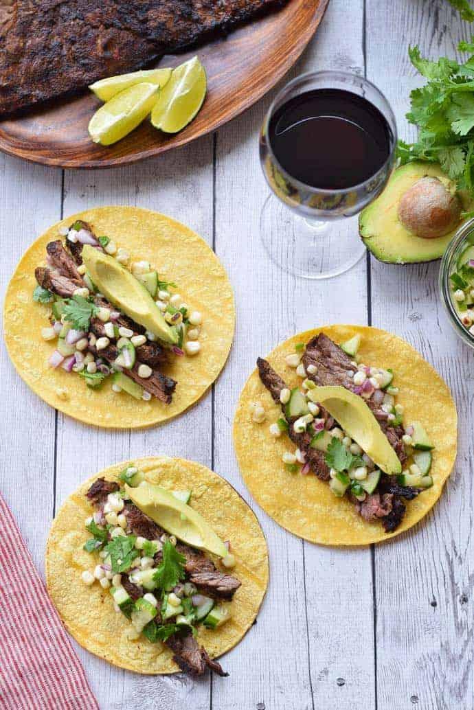 Three tacos on a wooden table with a bottle of wine.