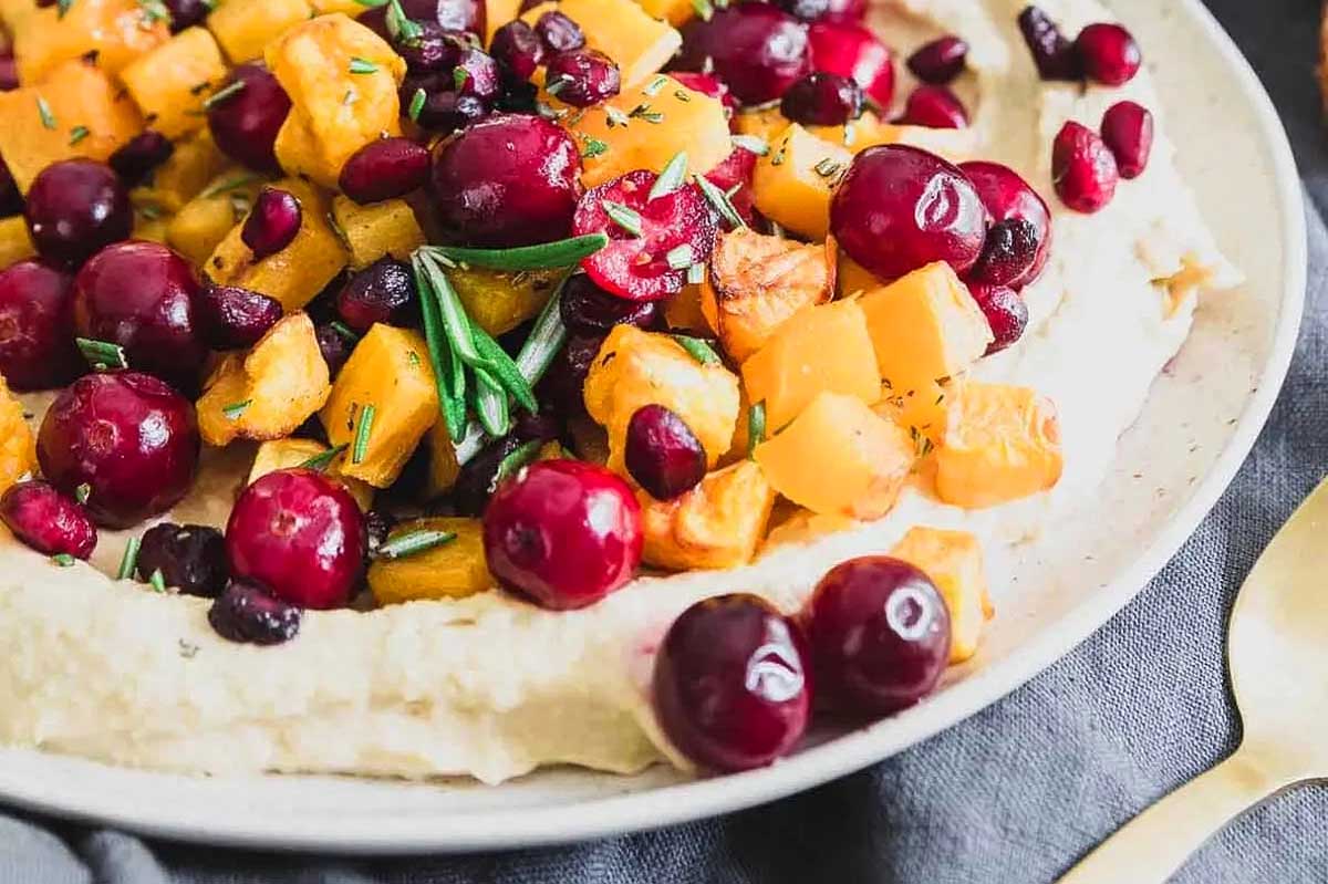A plate of hummus with cranberries and walnuts.