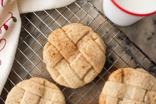 Three cookies on a cooling rack next to a glass of milk.