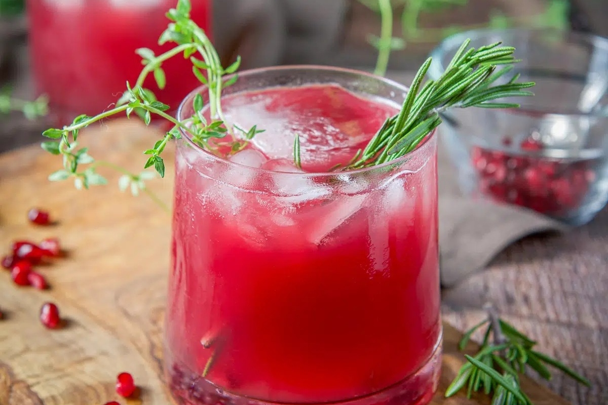 A festive glass of pomegranate cocktail with rosemary sprigs, perfect for Christmas celebrations.