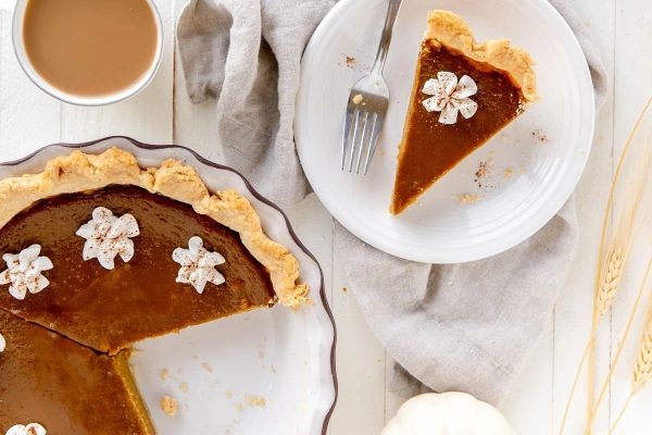 A slice of pumpkin pie on a plate with a cup of coffee.